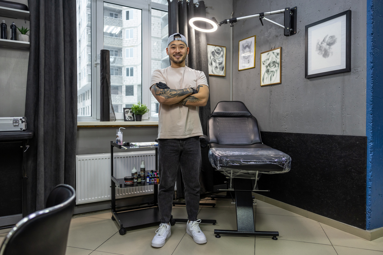 In the tattoo shop. Asian young man standing in front of his chair in tattoo shop. 