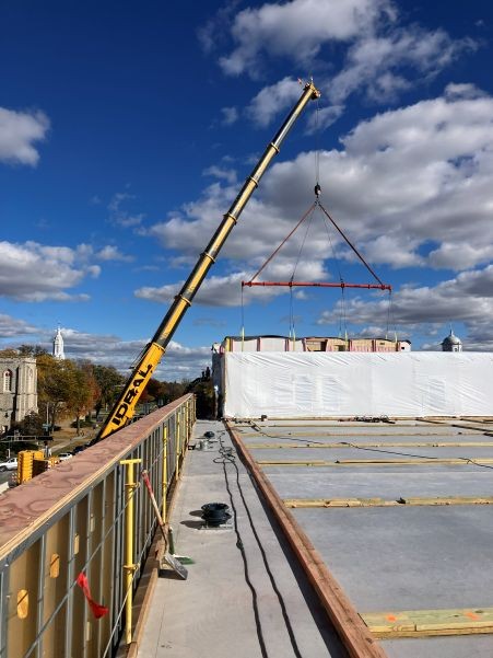 Crane placing pre-fabricated building on wood frames built on a concrete pad.