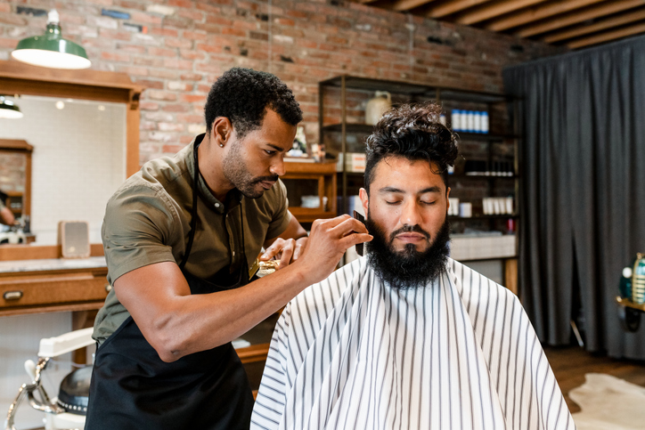 Barber trimming beard of the customer at a barbershop.