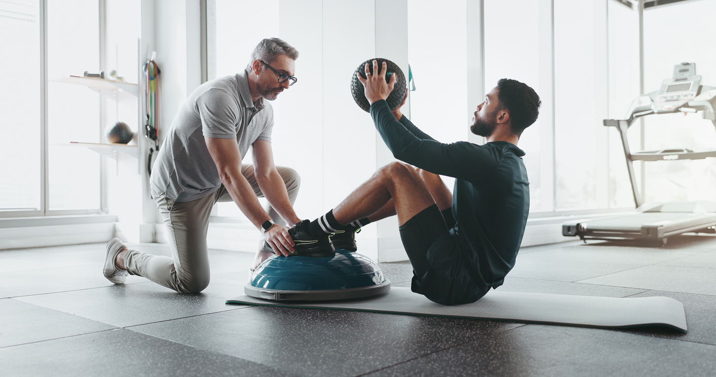 Athletic trainer, coaching client on work with medicine ball in a professional gym and fitness setting. 

