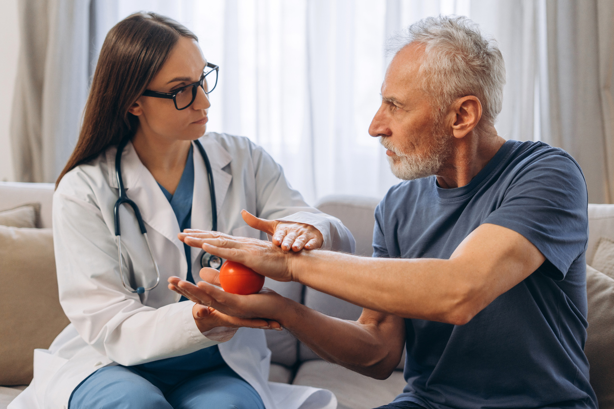Female therapist assisting a senior man with a red stress ball, performing hand therapy exercises for rehabilitation and recovery.

