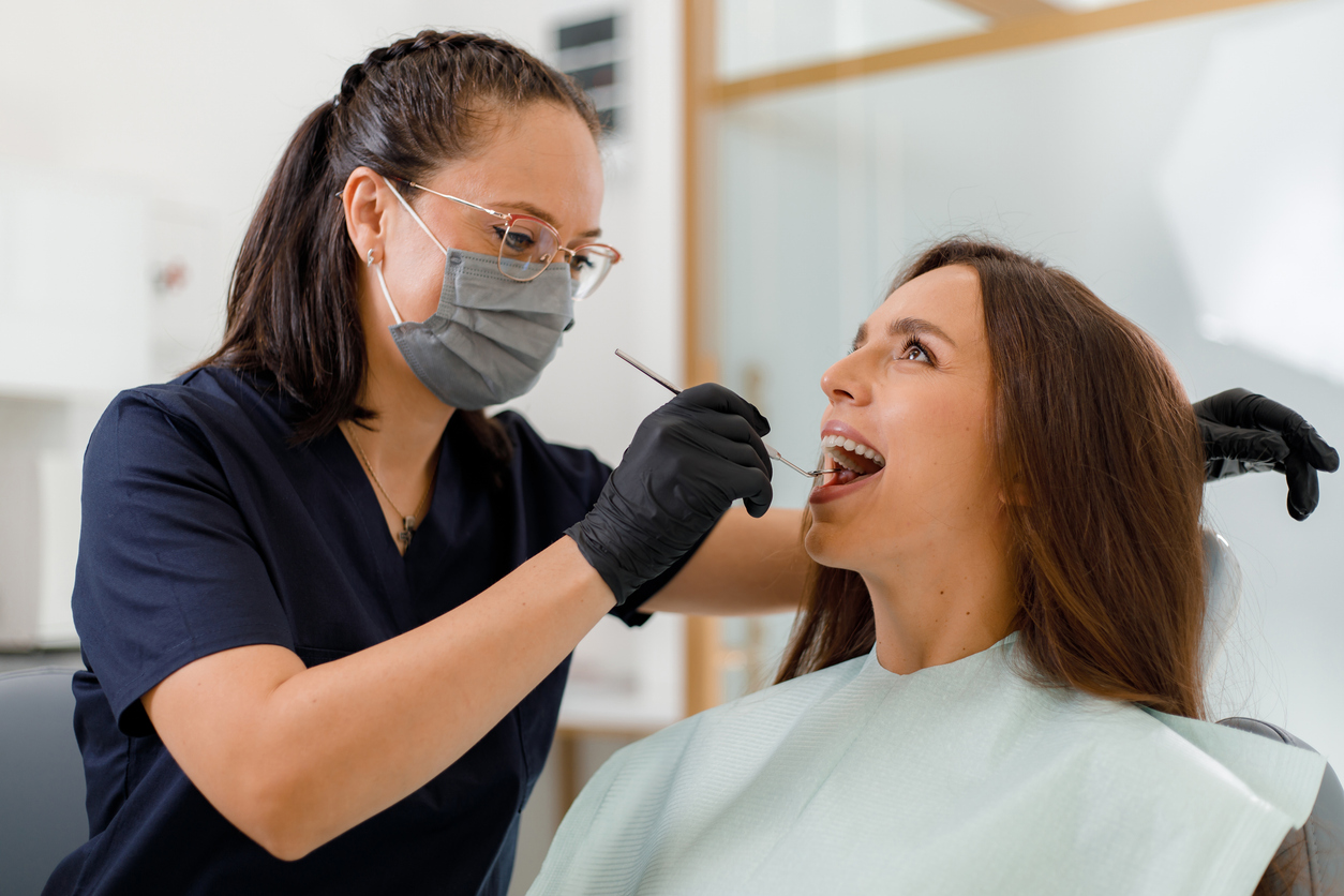 A dental hygienist carefully examines a patient's teeth during a routine check-up at a clinic. The patient sits comfortably in the dental chair, engaged in the process.
