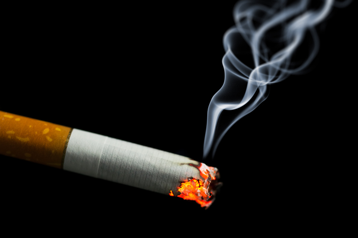 Burning cigarette with smoke on black background.