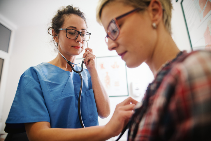 Female middle-aged doctor using stethoscope to examine patient image.