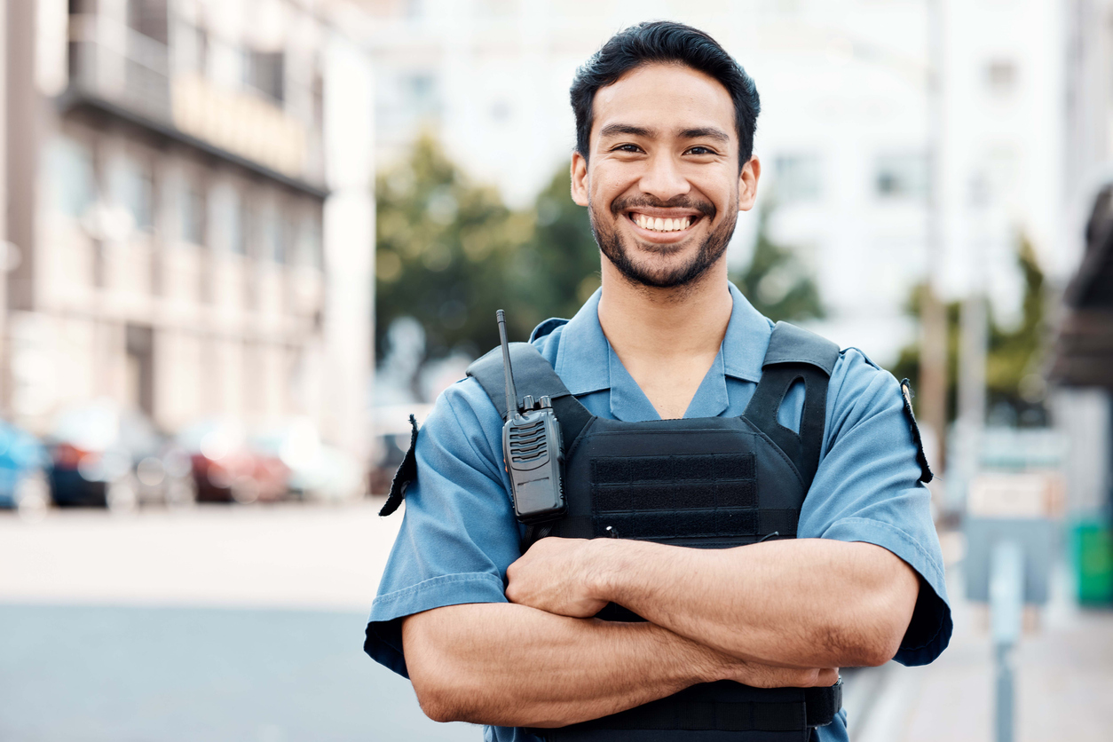 Smiling Asian man in city with arms crossed for security or street safety.