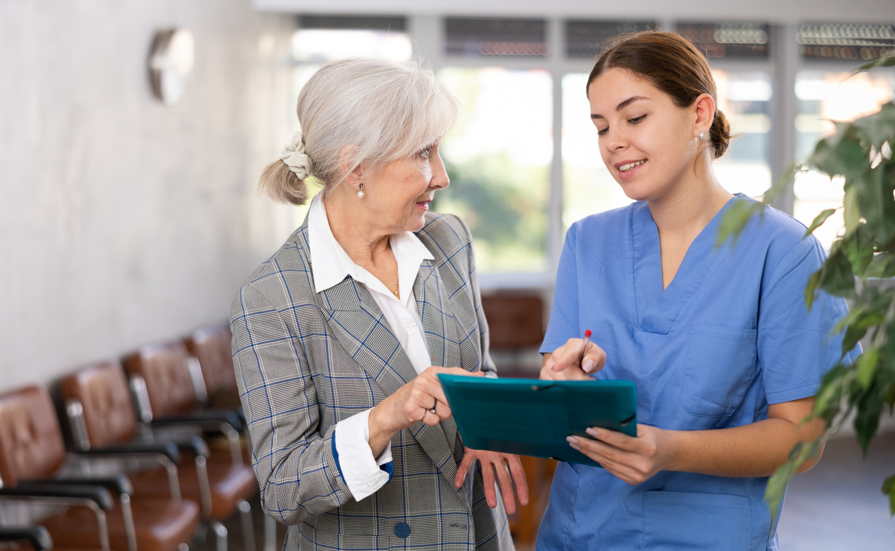 Young woman in medical uniform and older woman in business suit look at folder with documents.

