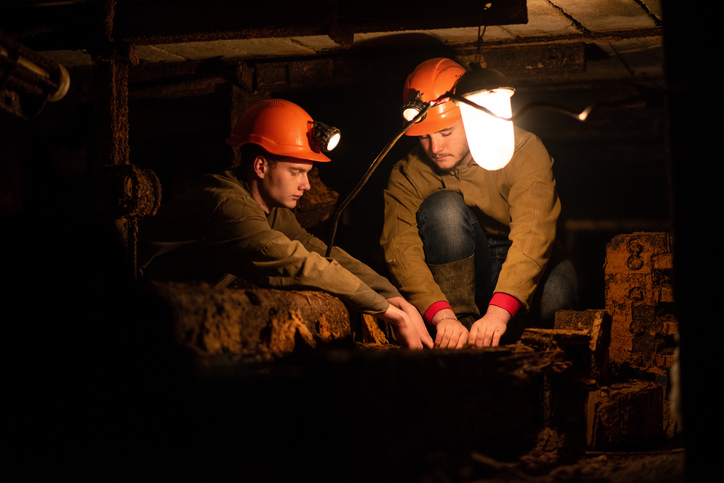 Two young guys in a working uniform and protective helmets sitting in a low tunnel mine.
