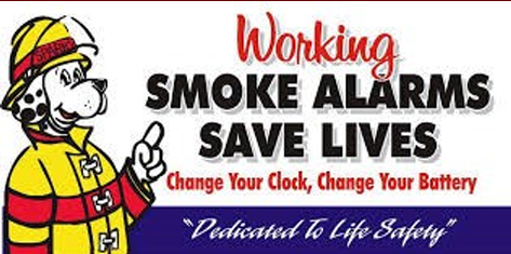 Dog in a firefighter outfit pointing at text that says "Working Smoke Alarms Saves Lives Change Your Clock, Change Your Battery Dedicated to Life Safety"