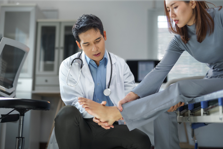 Doctor examining a female patient's injured foot during a consultation in a medical office. 