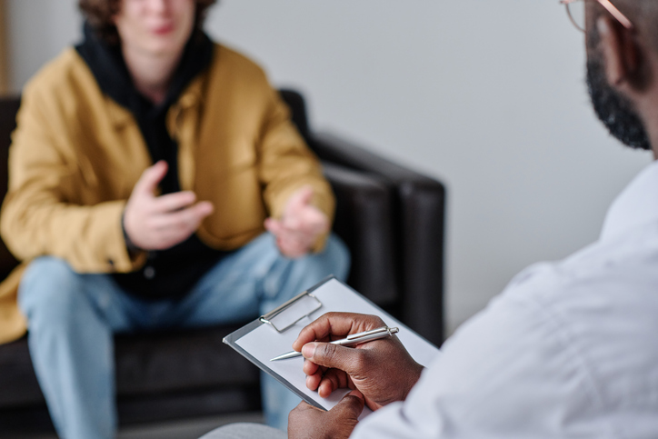 Psychologist listening to patient and making notes during psychotherapy session.

