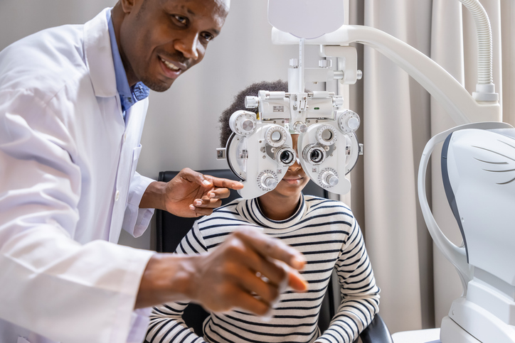Young girl doing eye test checking examination with optometrist using phoropter in clinic.