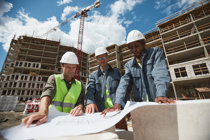 Portrait of three workers discussing floor plans at commercial building construction site.