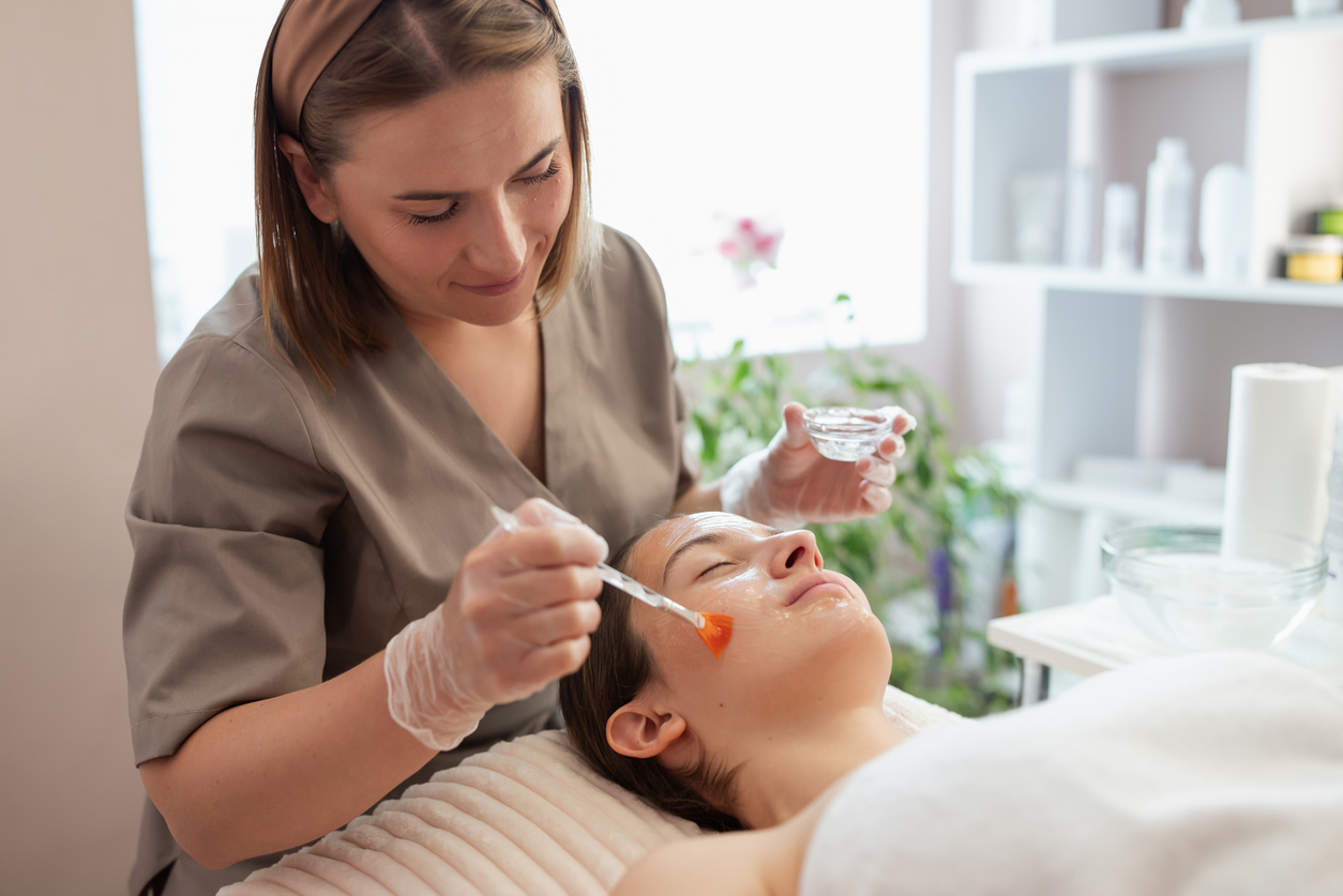 Aesthetician applying gel on woman's face with brush.