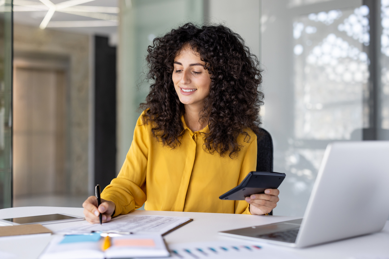 Latin American businesswoman accountant at office desk with calculator, pen, and laptop. 