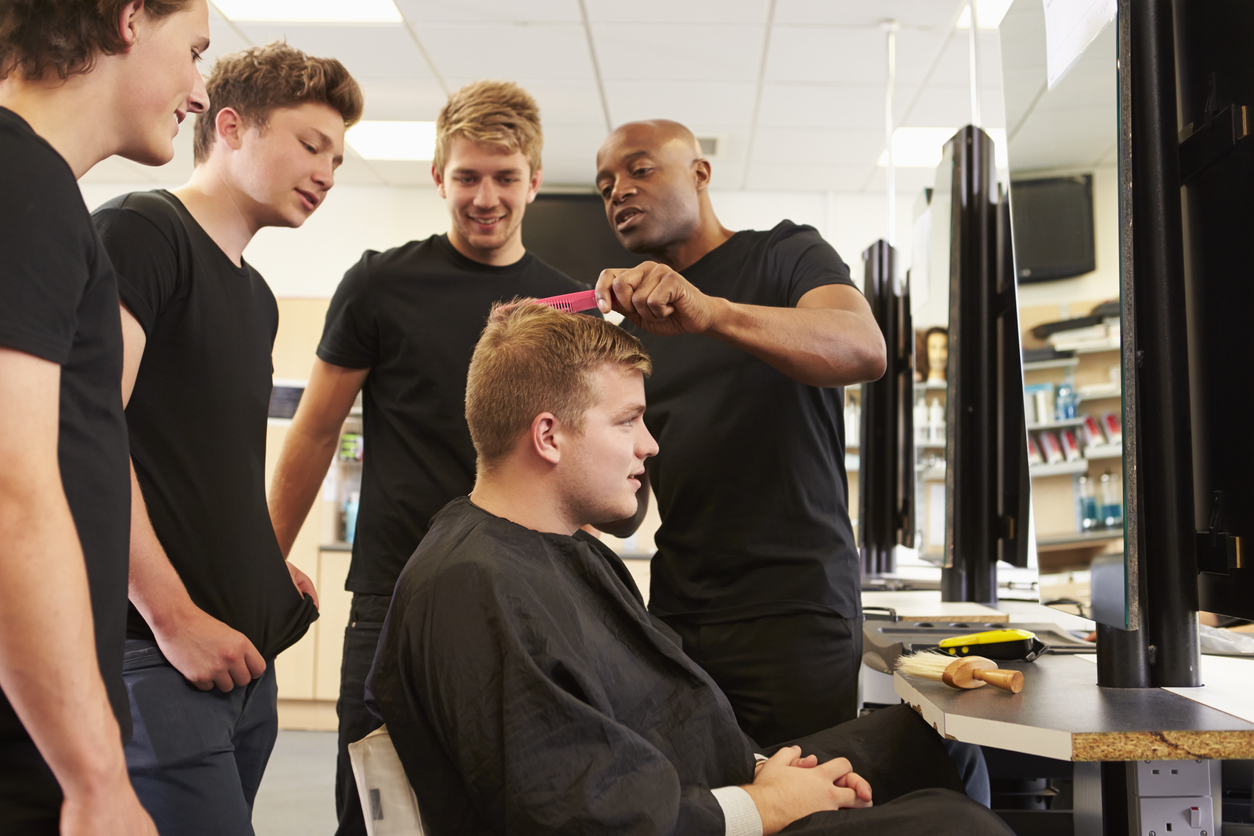 Teacher Helping Male Students Training To Become Barbers. 