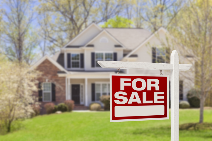 Home For Sale Real Estate Sign in front of a two-story white and brick house with green lawn.