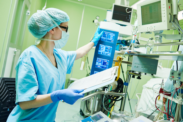 Surgery assistant perfusionist operating a modern heart lung machine with artificial cardiac valve at operating room in cardiology clinic.