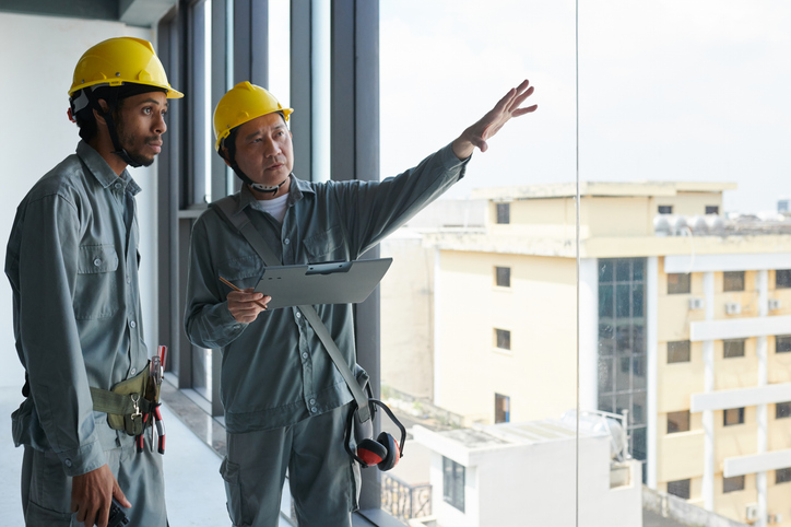 Two construction workers looking out the window and talking about building plans. 