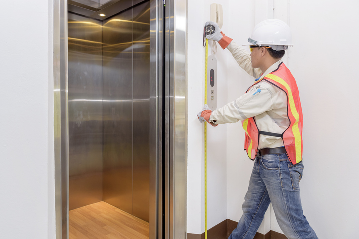 Engineer investigating height of mechanism that lifts the elevator with a ruler. 