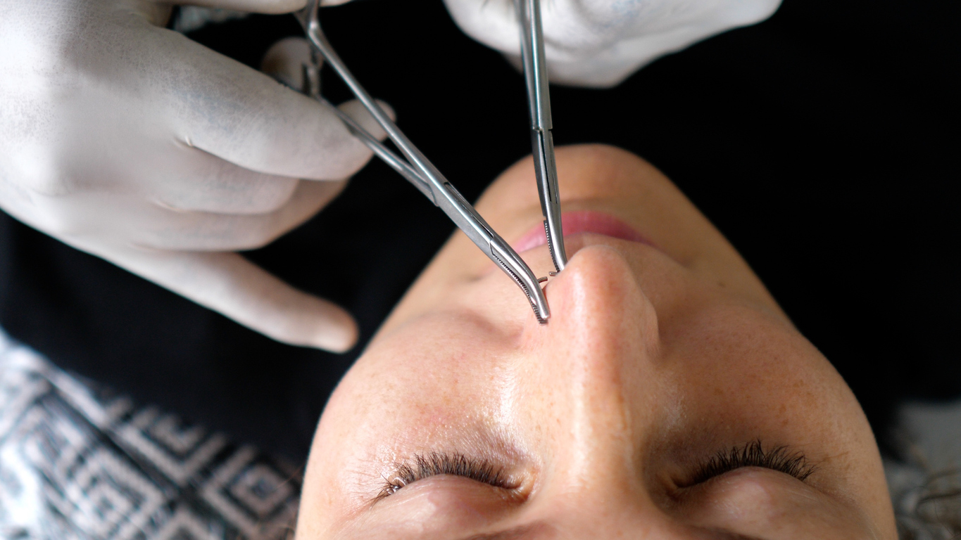 Body piercing process. Professional piercer in the disposable gloves sets nose ring properly.