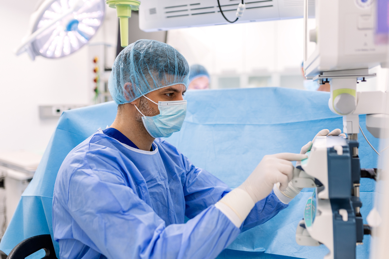 Anesthesiologist in blue scrubs and mask monitoring patient vital signs