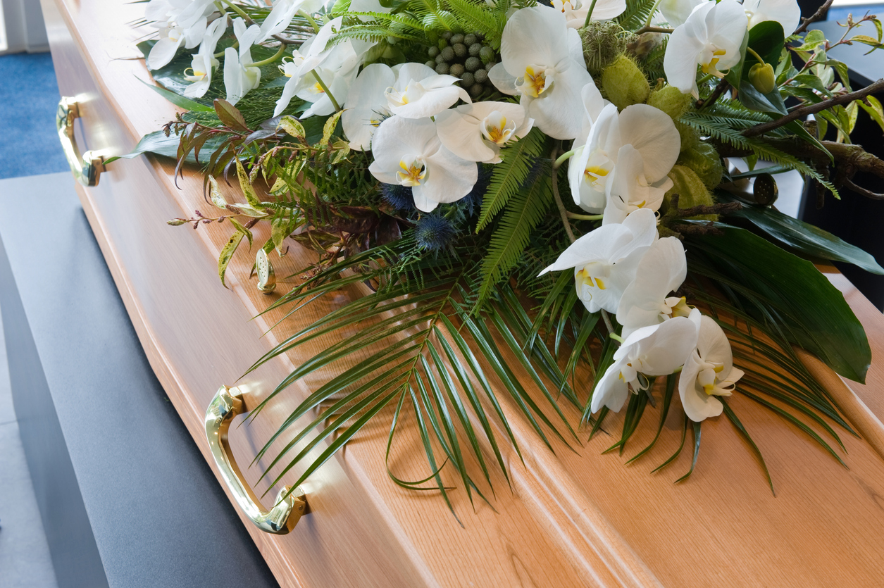 A wooden coffin with a white flower arrangement. 

