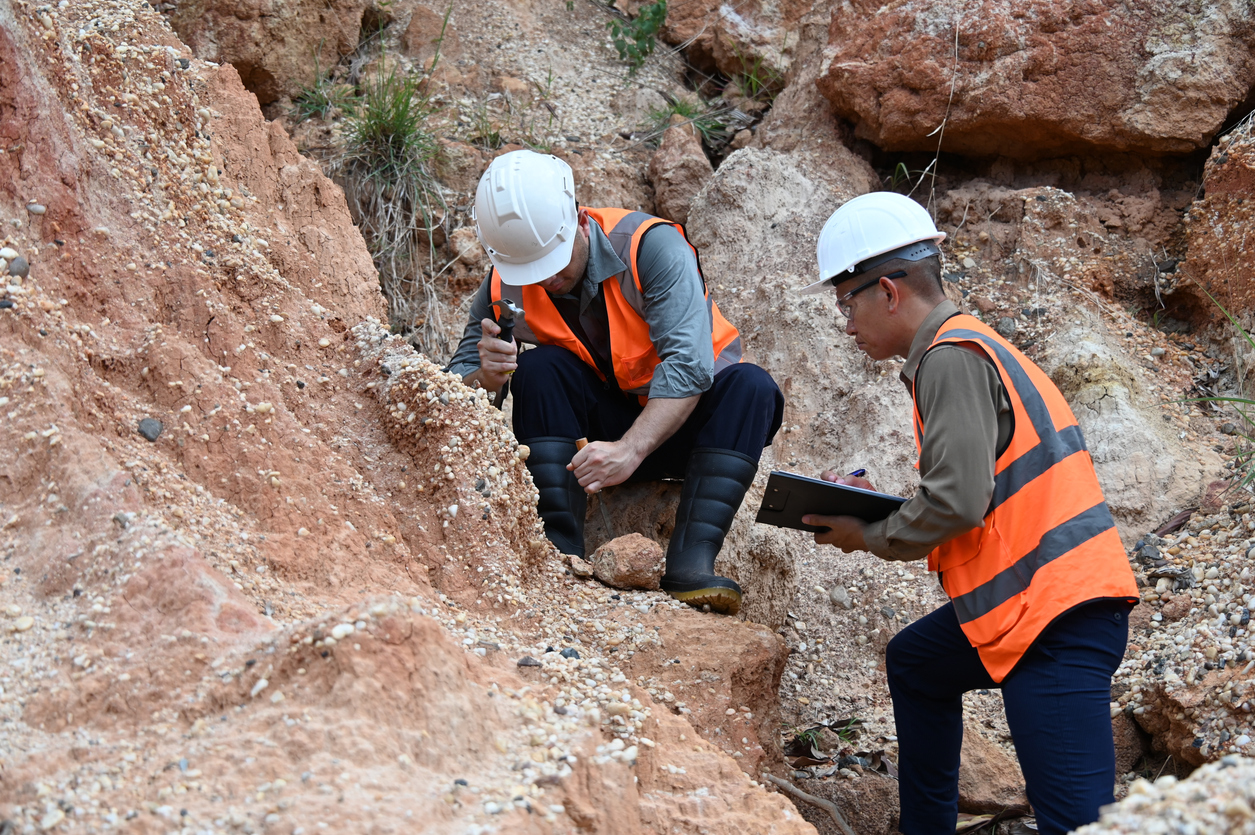 Two male geologists inspecting soil and rock formations at an excavation site.
