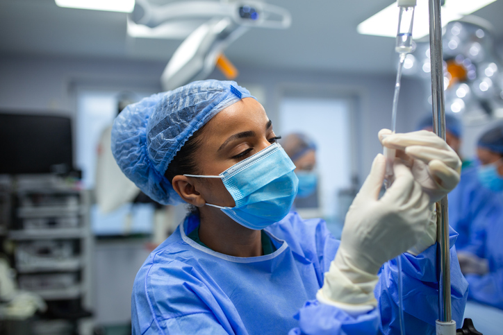 Female anesthesiologist adjusts IV drip in sterile operating room. 