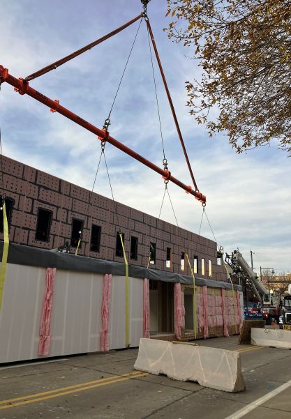 Pre-fabricated building being lowered by crane on top of another pre-fabricated building on an asphalt street in Milwaukee, WI.